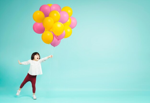 Little girl holding helium balloons on plain background