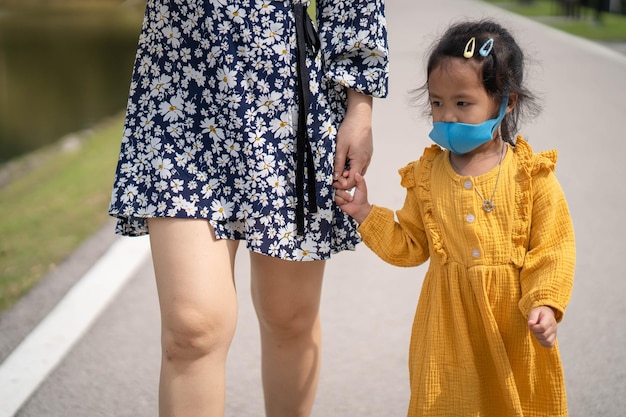 Little girl holding mothers hand wearing healthy face mask walking on the road