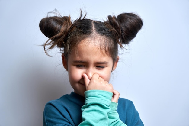 Little girl holding nose to avoid disgusted smell pinches nose with fingers and holding breath isolated on white background