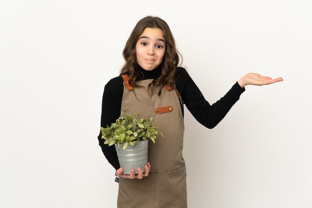 Photo little girl holding a plant isolated on white background having doubts while raising hands