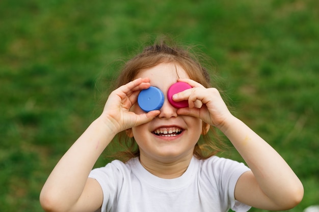 Little girl holding plastic bottle caps on her eyes