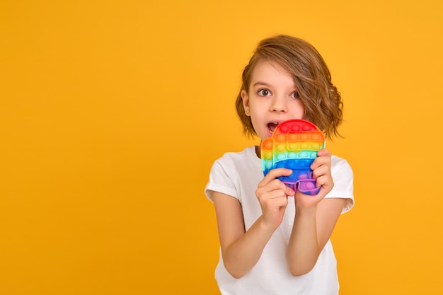 Little girl holding pop it antistress toy on yellow