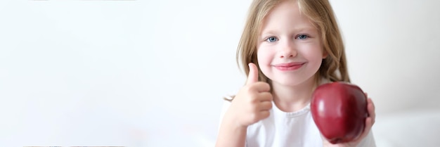 Little girl holding red apple in her hands and showing thumbs up