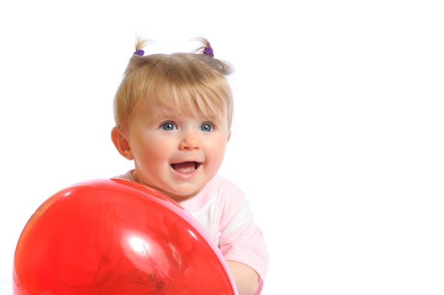 Little girl holding red balloon in hands and smiling, surprised expression on face. Photo of baby isolated on white background