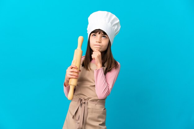 青い背景で隔離の麺棒を持って見上げる少女