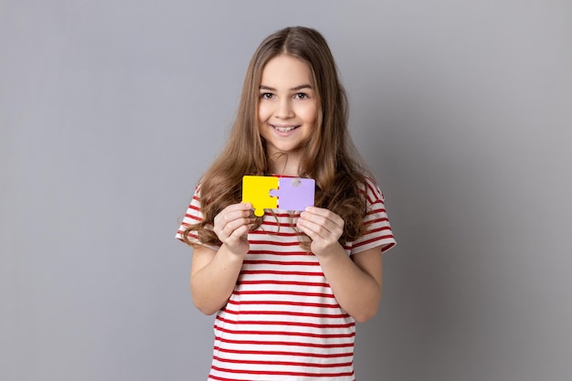 Little girl holding and showing two jigsaw puzzle pieces matching and connecting puzzles