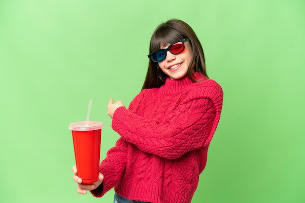 Little girl holding soda over isolated chroma key background pointing back