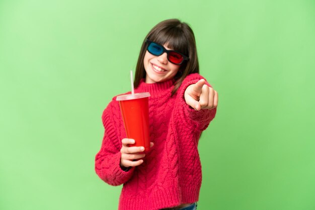 Little girl holding soda over isolated chroma key background pointing front with happy expression