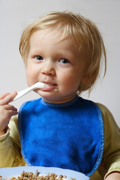 Little girl holding a spoon at her arms and eating a pap