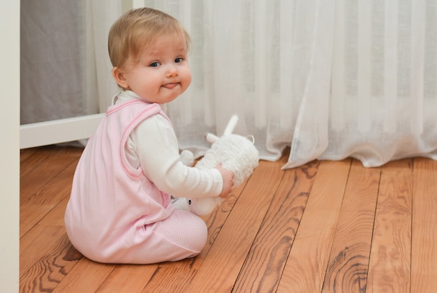 Маленькая девочка держит игрушку в руках и показывает язык