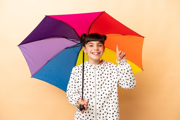 Little girl holding an umbrella isolated on beige wall pointing up a great idea