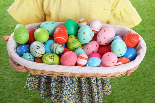 Little girl holding wicker basket full of Easter eggs outdoors closeup