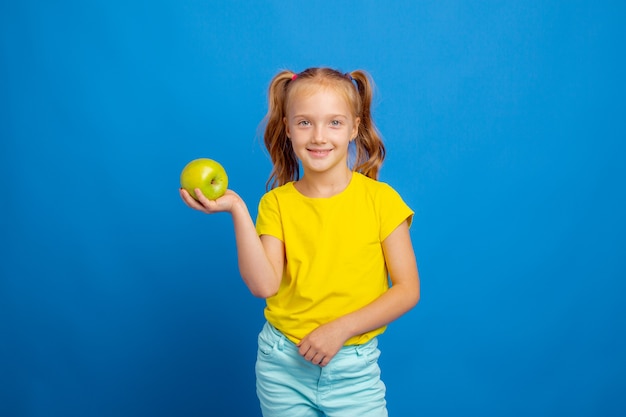 A little girl holds an apple on a blue background