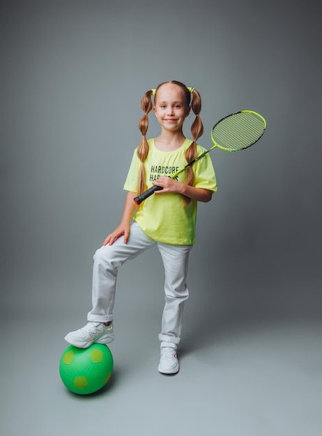 A little girl holds a ball and a racket on a gray background The concept of professional sports sportsthemed poster greeting cards headlinessport