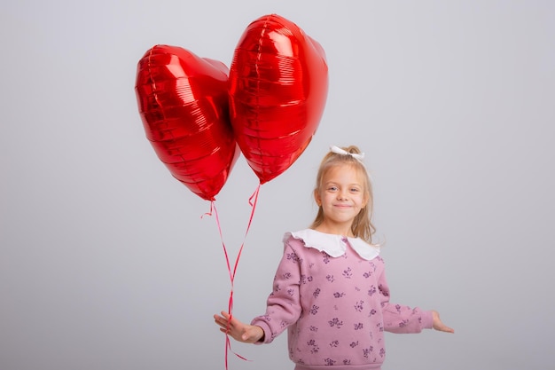 little girl holds balloons in the shape of a heart  on a white background a gift for Valentines