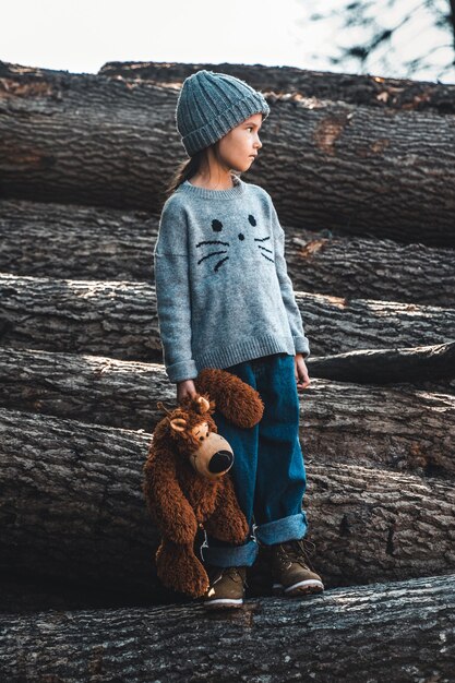 Little girl holds a bear in her arms on wooden logs