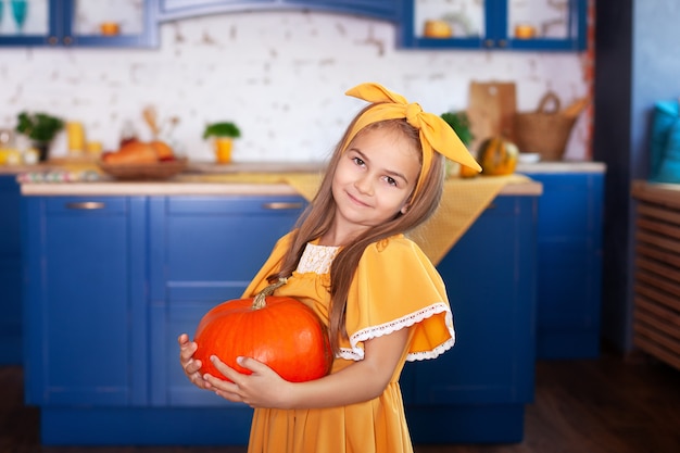 Little girl holds big pumpkin in kitchen at home. Harvesting. Healthy nutrition, vegetarianism, vitamins, vegetables.