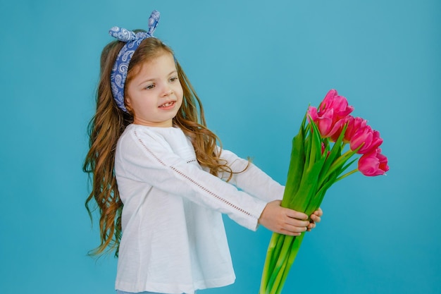 A little girl holds a bouquet of pink tulips on a blue background