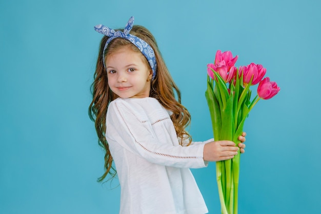 A little girl holds a bouquet of pink tulips on a blue background