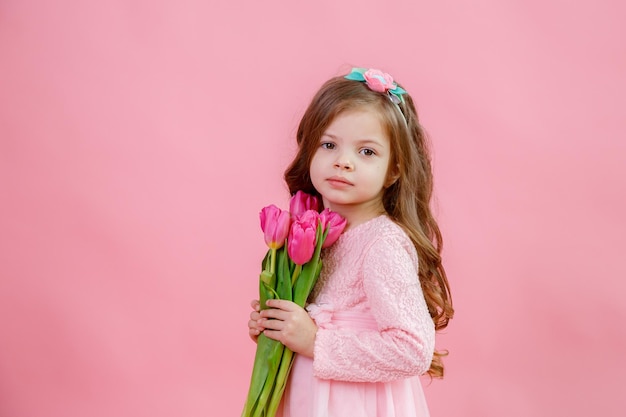 A little girl holds a bouquet of pink tulips on a pink background