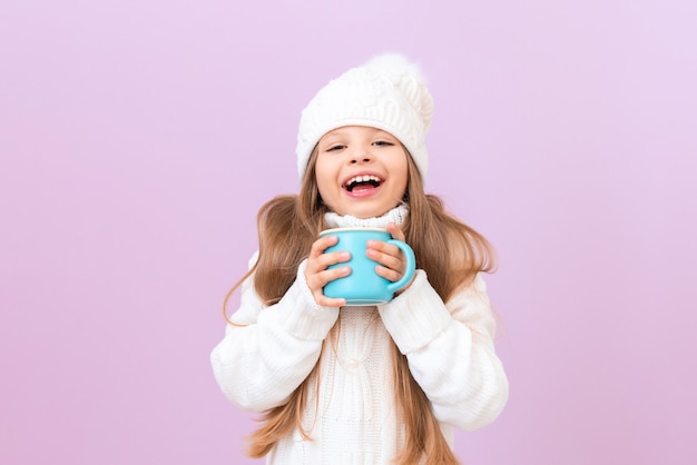 A little girl holds a cup of hot drink and smiles.