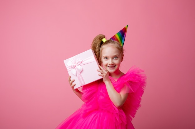 A little girl holds a gift on a pink background celebrating her birthday