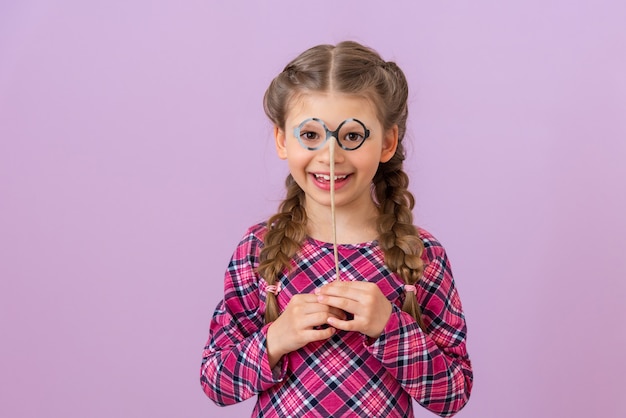 A little girl holds a pair of fancy dress glasses near her face.
