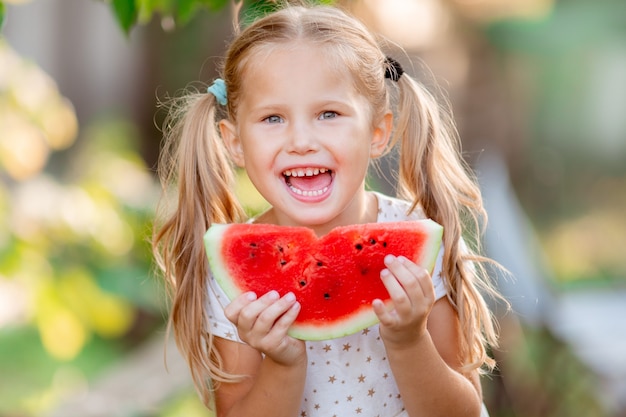 A little girl holds a piece of watermelon in the summer sun