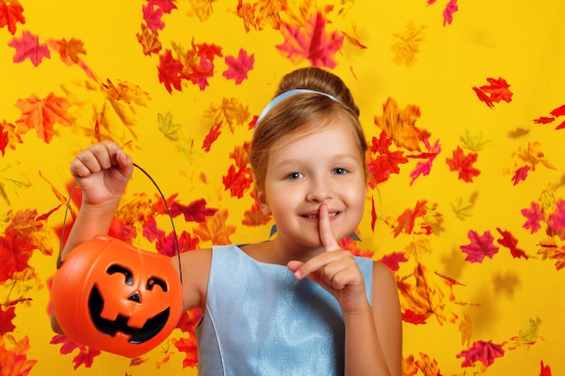 Little girl holds a pumpkin jack bucket and shows a shh sign.