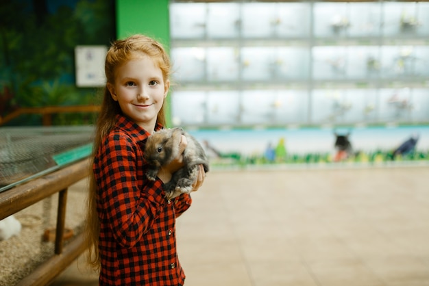 Little girl holds rabbit in hands, pet store. Child buying equipment in petshop, accessories for domestic animals