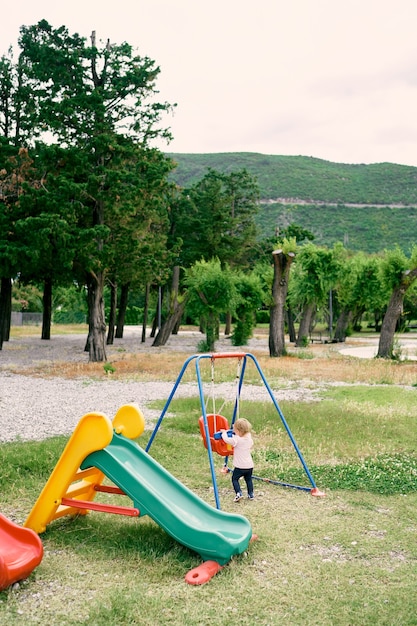 Little girl holds on to a swing in the park with her hands side view