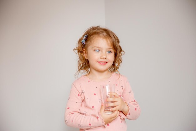 A little girl at home holds a glass of water recommends