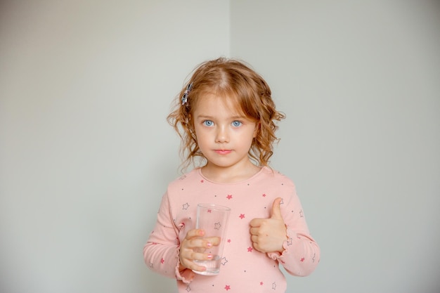 집에 있는 어린 소녀가 물 한 잔을 들고 있습니다.