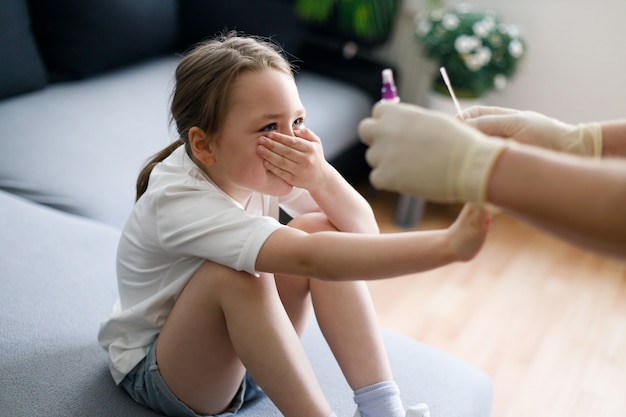 Little girl at home during taking nasal mucus test sample from nose performing respiratory virus testing procedure showing Covid-19