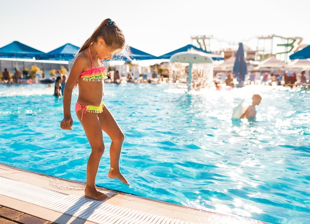 A little girl in a hot pink bathing suit stands by the pool with clear transparent water