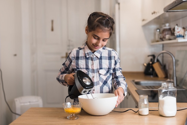 Foto casalinga della bambina che cucina in cucina, agitando una crema con un mixer in una ciotola. mixer pasticceria da forno torta di cottura torta di mele, rendendo.