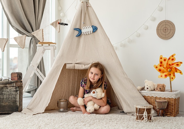 Bambina che abbraccia l'orsacchiotto della peluche in wigwam