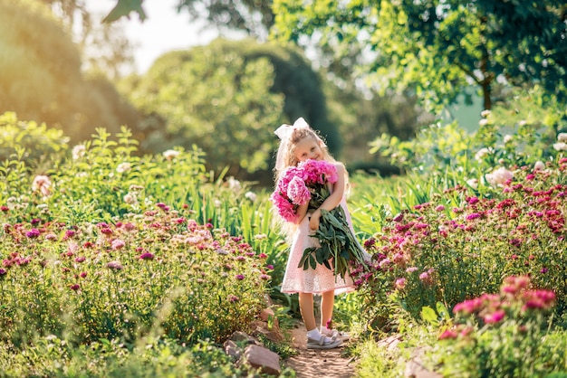 La bambina abbraccia un grande mazzo di peonie. un bambino con i fiori rosa