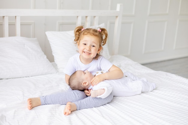 A little girl hugs a newborn sister or brother on a white bed at home two children in the family