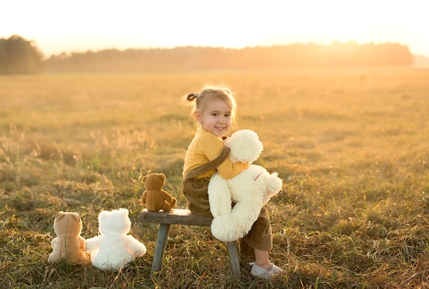 A little girl hugs one of the teddy bears in a field at sunset
