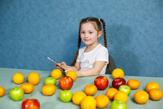 Фото Маленькая девочка в белой футболке держит в руках планшет и изучает фрукты