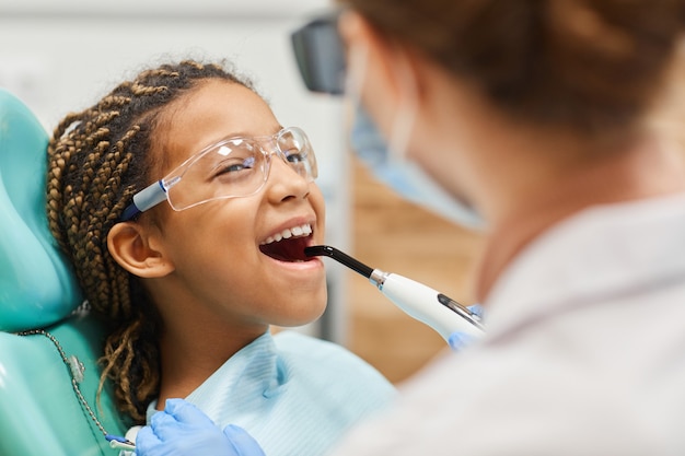 Фото Маленькая девочка в защитных очках открывает рот, пока дантист лечит зубы в больнице