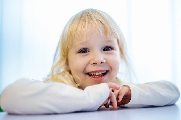 Фото Маленькая девочка в белой одежде смотрит в камеру и улыбается.