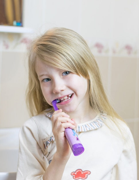 A little girl is brushing her teeth with an electric toothbrush.