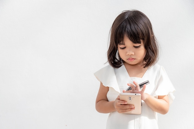 Маленькая девочка сосредоточена на телефоне, посмотрите на смартфон, концепция технологии для детей, вид профиля, изолированные на белом фоне, скопируйте пространство