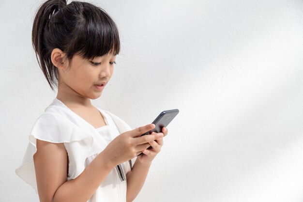 小さな女の子は子供のためのスマートフォン技術の概念を見て電話に集中しています