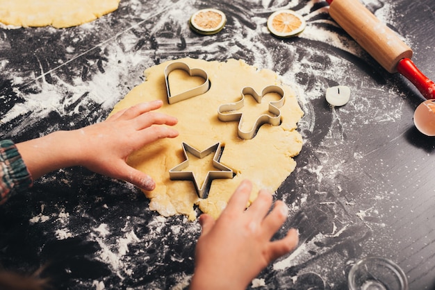 Little girl is cutting forms from gingerbread dough with metalic form.