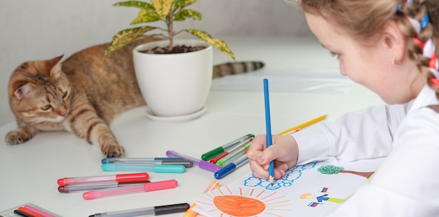 Photo a little girl is drawing and a cat is lying on the table