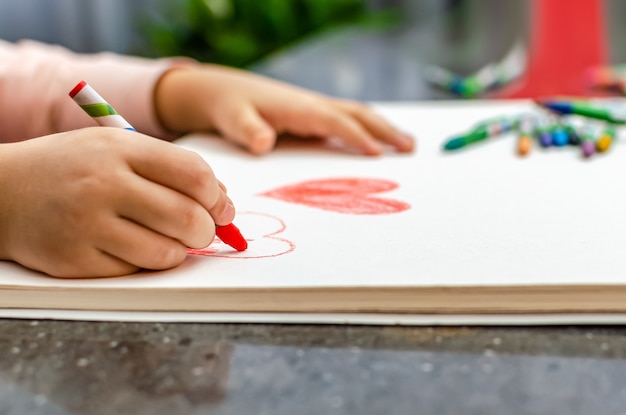 Foto una bambina sta disegnando un cuore con gesso rosso - immagine ad alto angolo con messa a fuoco selettiva. concetto di san valentino