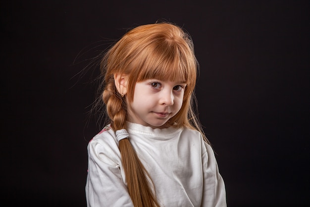 A little girl is embarrassed and costs eyes, a large portrait in a studio on a black background.